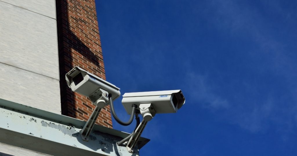Two outdoor security cameras mounted on a building against a clear blue sky.