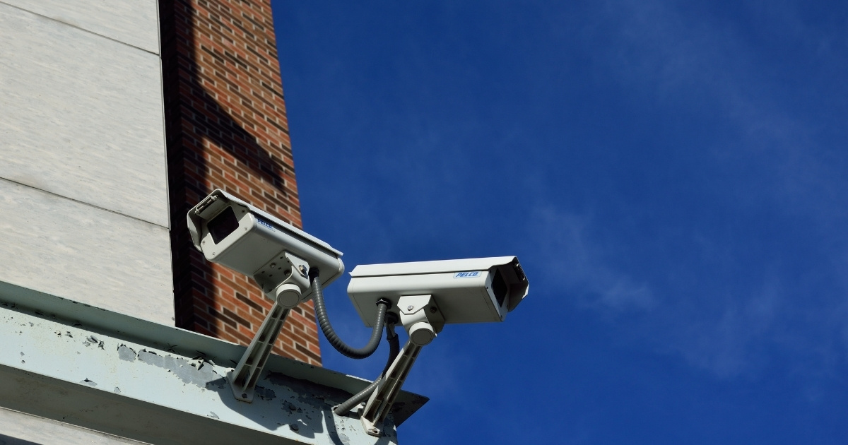 Two outdoor security cameras mounted on a building against a clear blue sky.