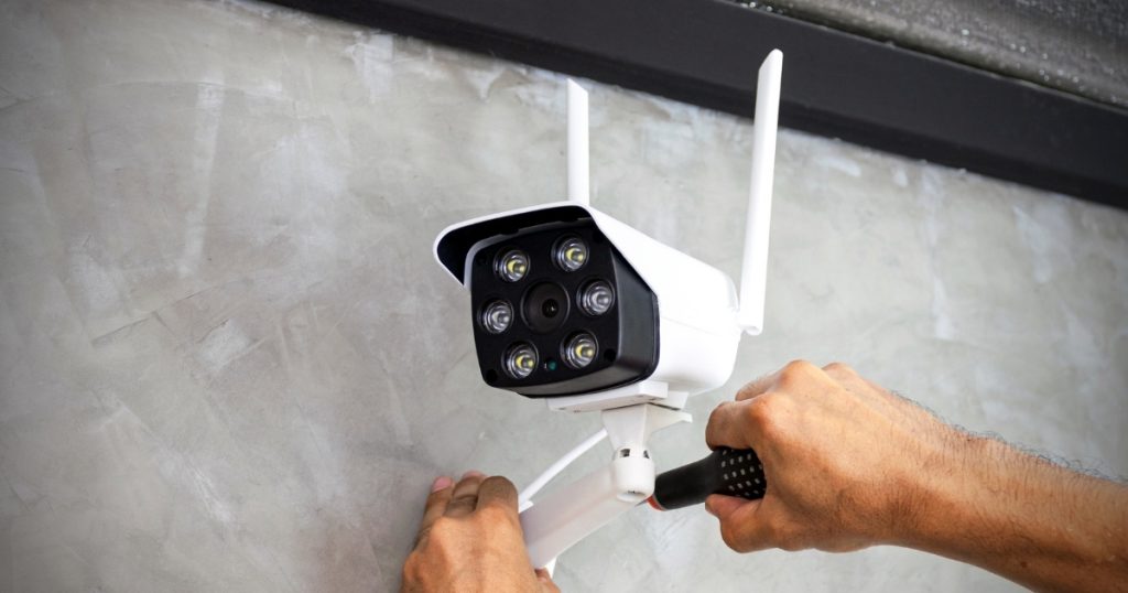 A technician installs a white CCTV camera on a concrete wall.
