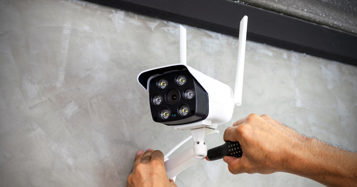 A technician installs a white CCTV camera on a concrete wall.
